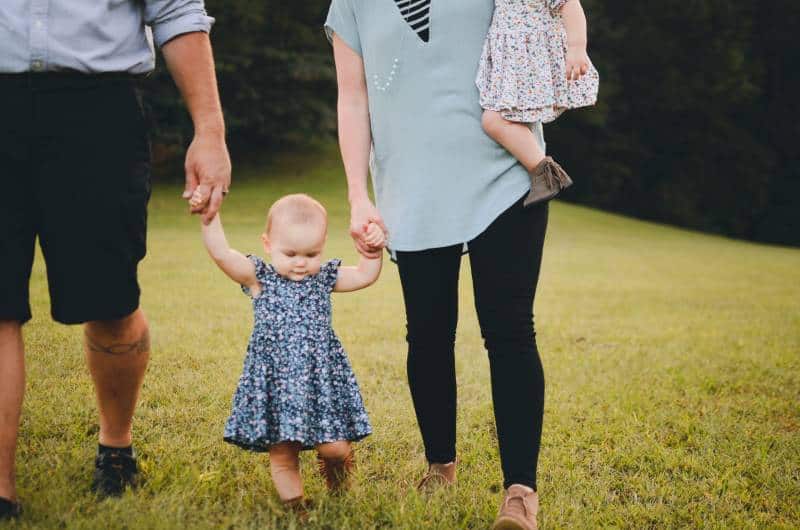 couple holding baby arm and walking on grass