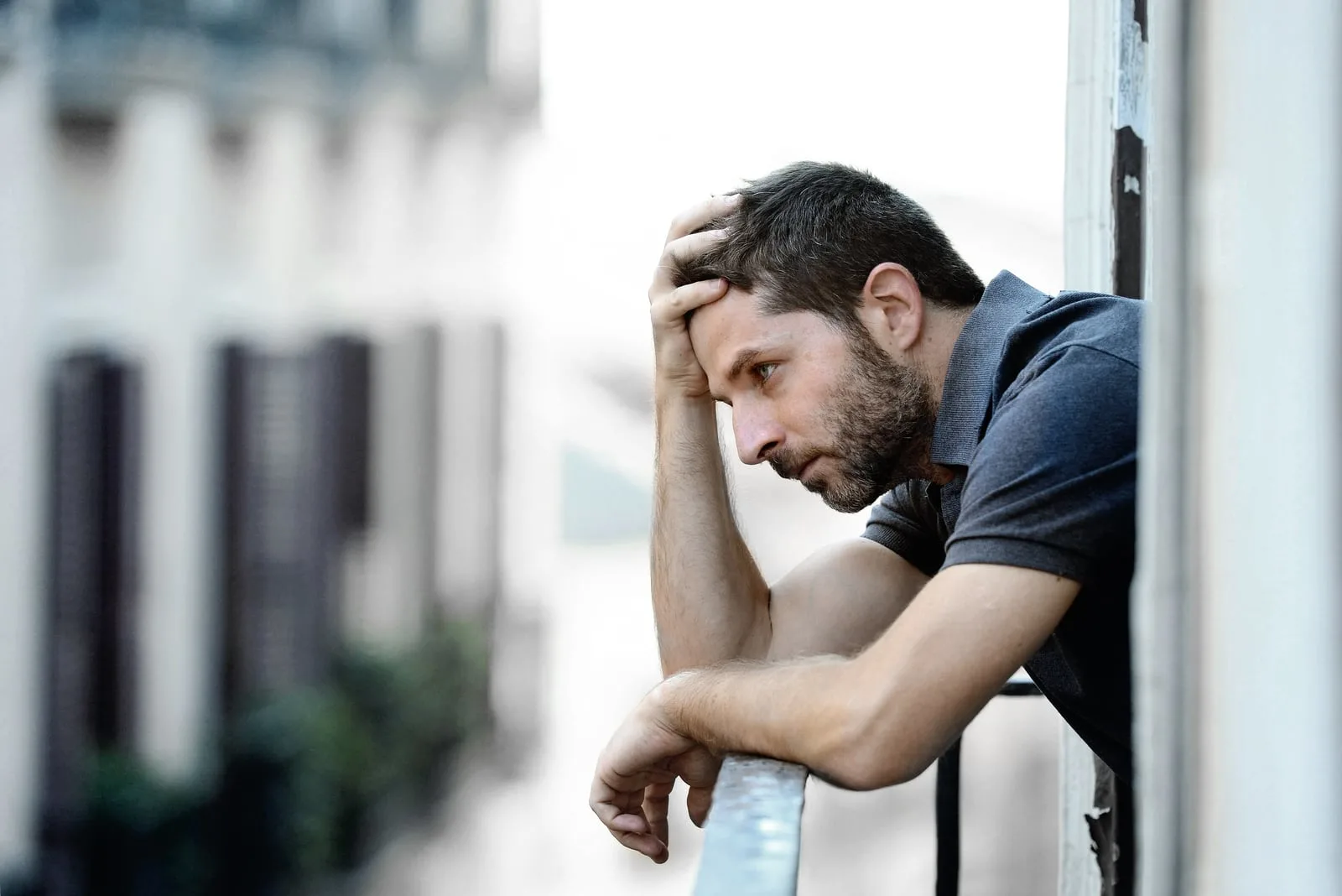 man outside at house balcony alone looking depressed