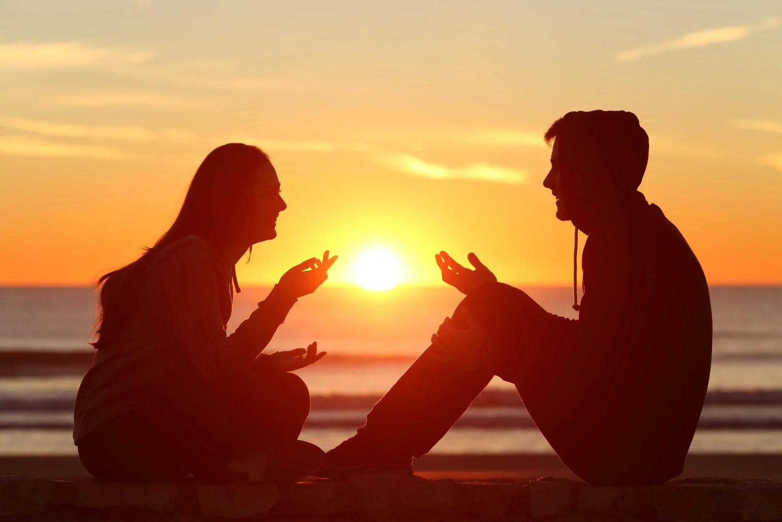 outside on a stone wall at sunset a man and a woman sit and talk