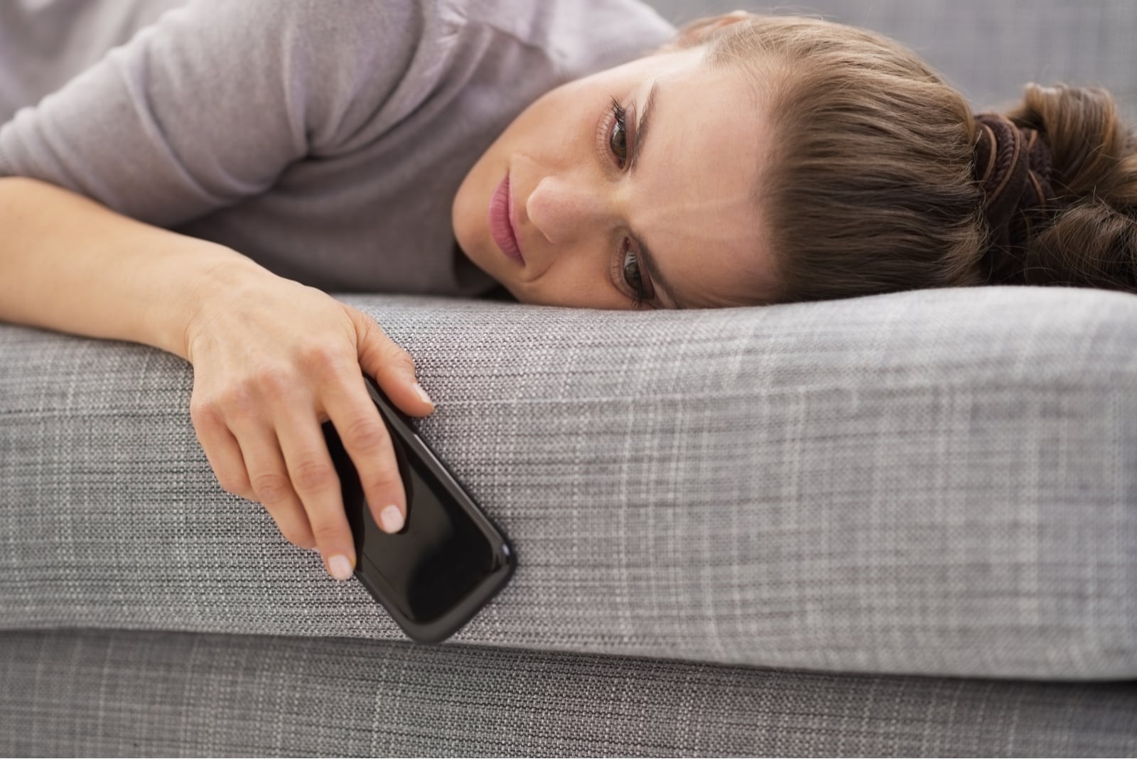 sad woman lying on a sofa holding phone