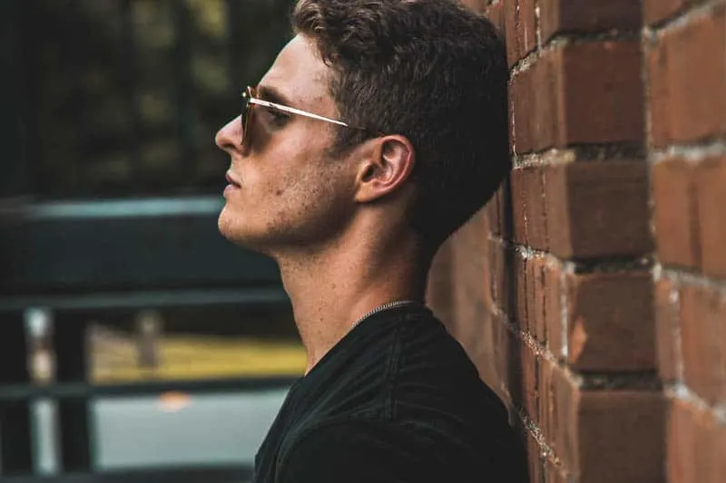 side view of man with sunglasses leaning on wall brick