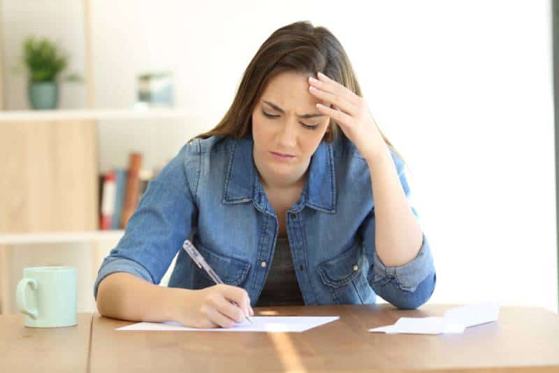 donna infelice che scrive su un foglio di carta a casa