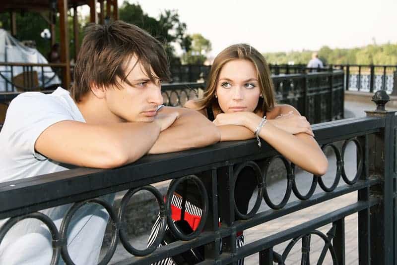 woman looking at man while leaning on fence