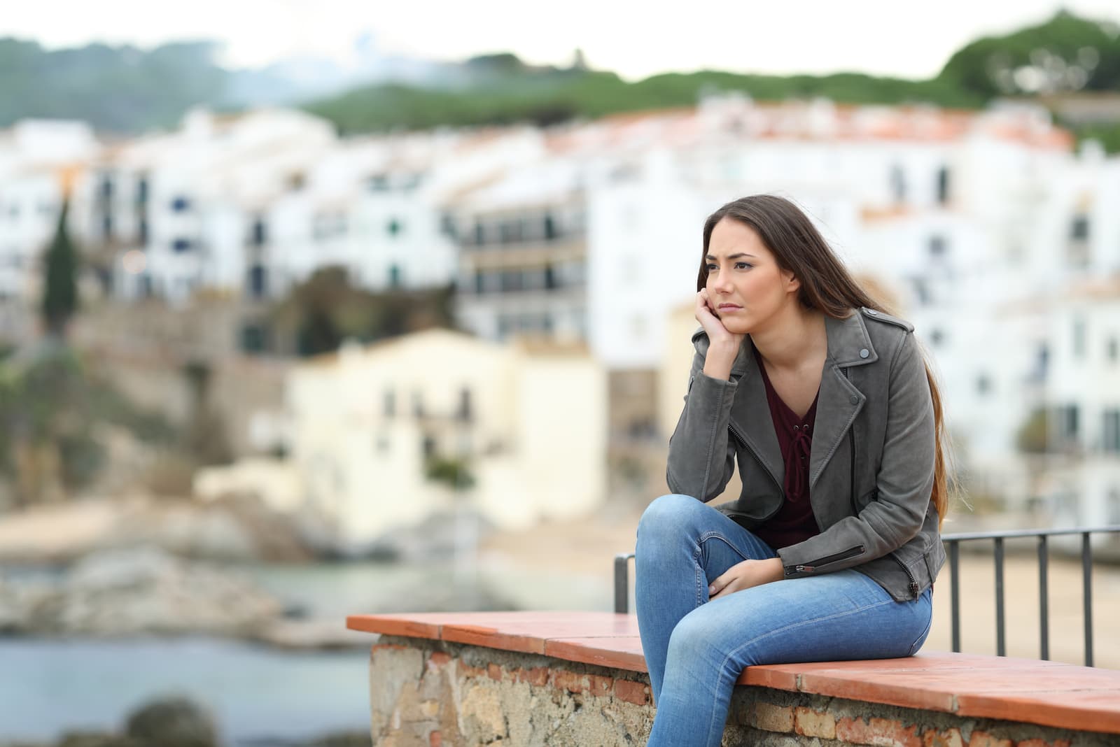 donna che guarda lontano seduta su un cornicione in una città costiera