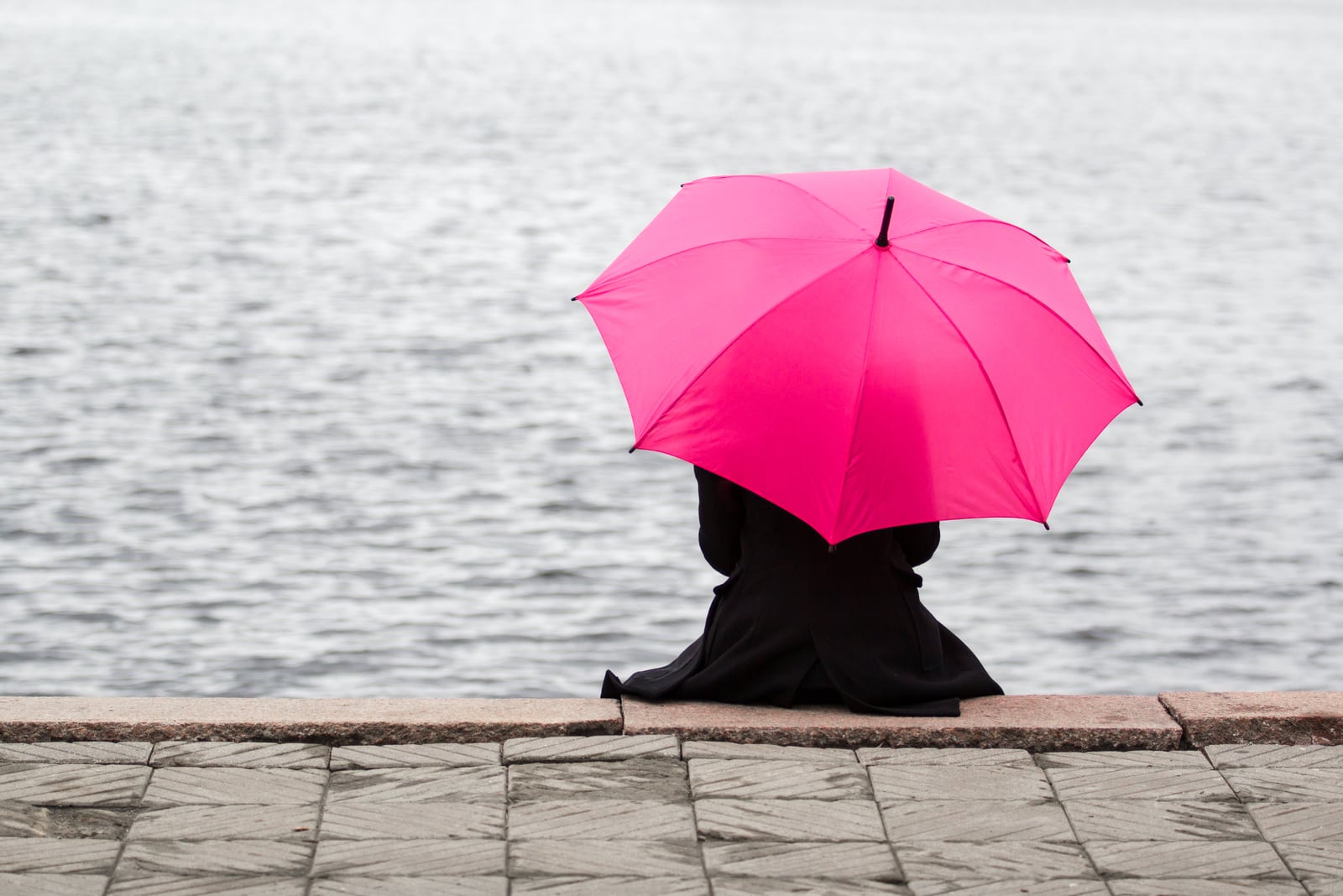 woman sitting alone holding pink umbrella