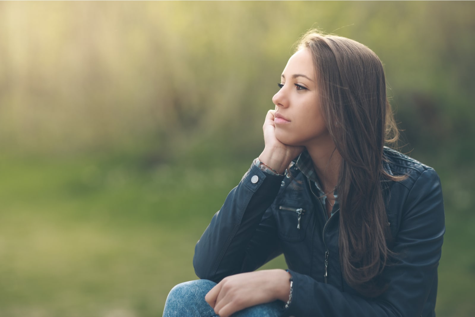 young pensive brunette woman sitting in nature