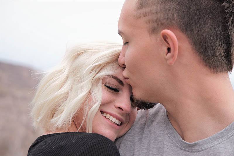 man kisses smiling blonde woman in forehead