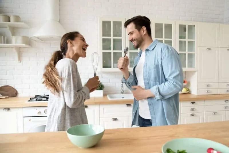 Funny young couple singing into kitchen ware microphones in the kitchen