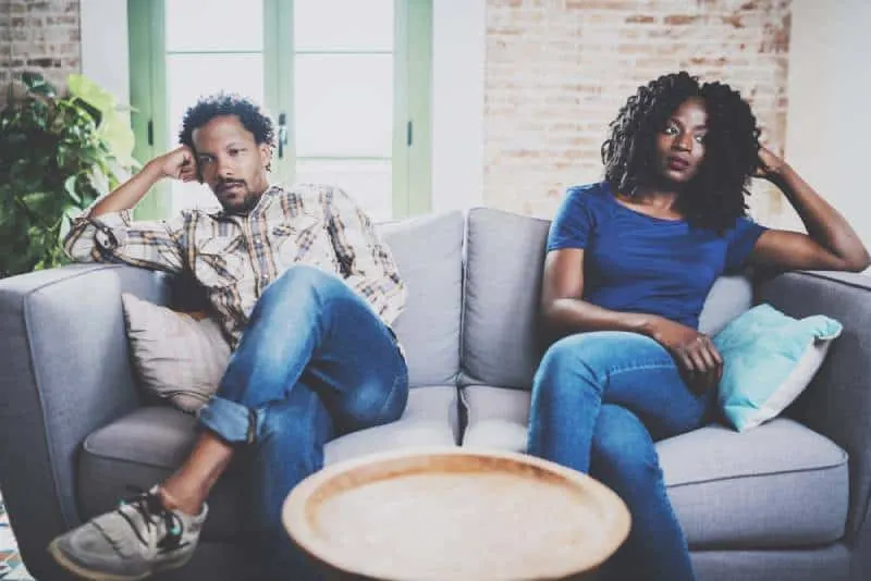 Men argue with his girlfriend, who is sitting next to him on the couch