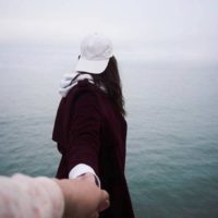 man holds woman hands while she facing sea
