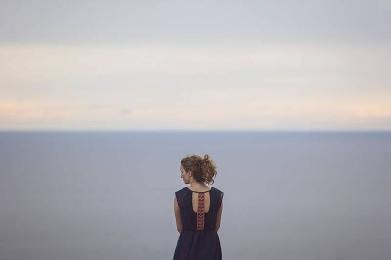 back view of woman sitting alone in front of sea