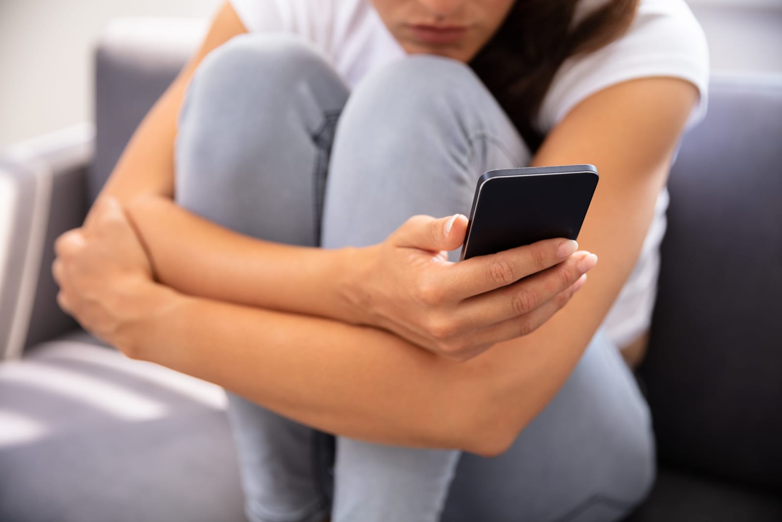 Young Woman Sitting On Sofa Using Smartphone