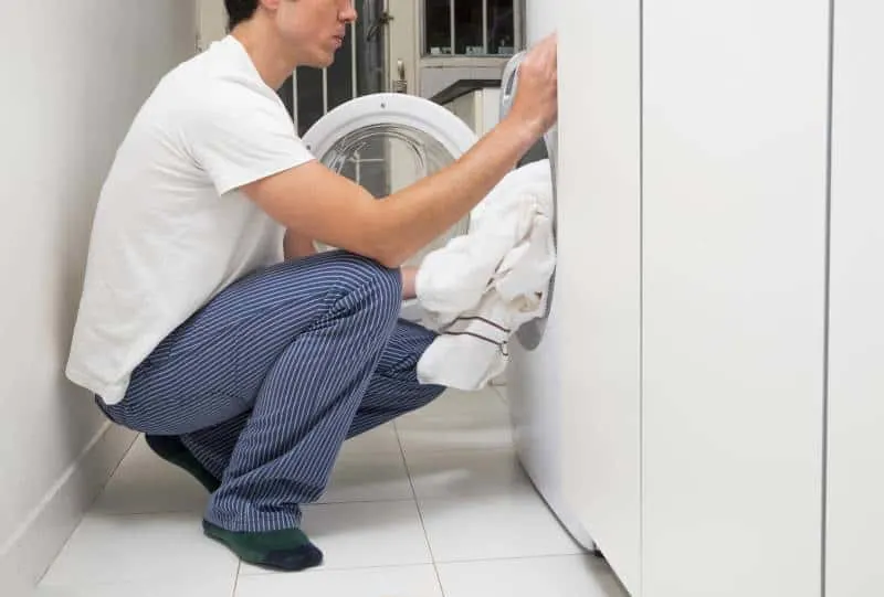 close up man putting clothes washing machine