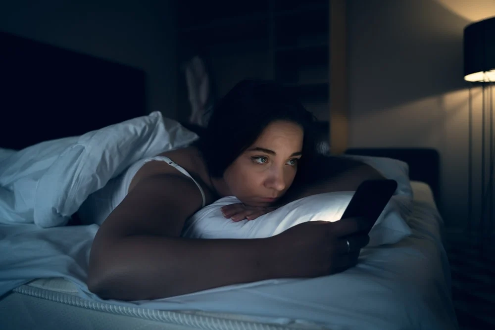 in the evening a sad brunette lies in bed and uses a cell phone