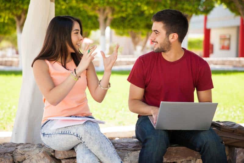 man holding laptop and talking to woman