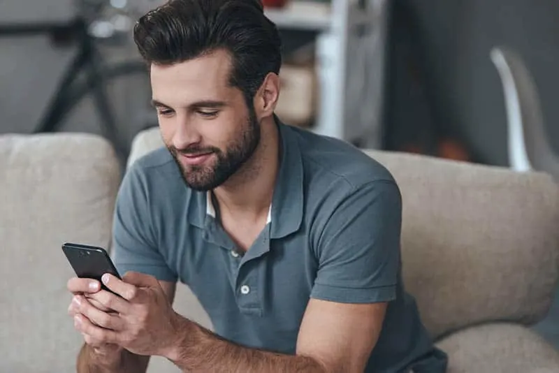 man typing on his phone while sitting at sofa