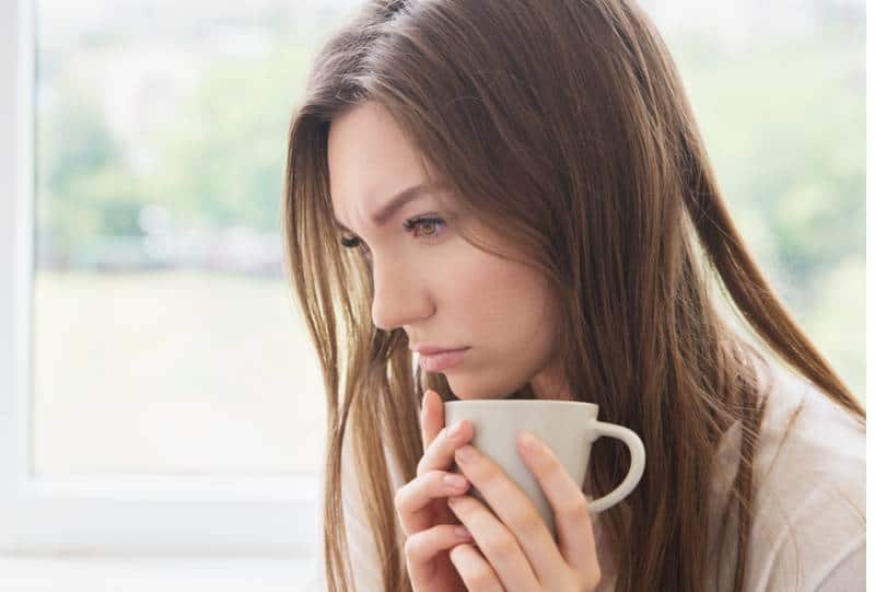 mulher triste com uma chávena na mão e a pensar em casa