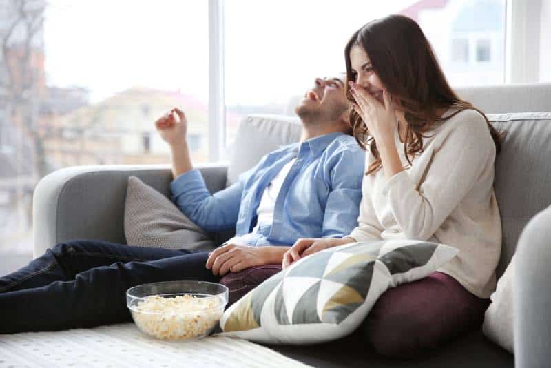 casal sorridente a ver televisão num sofá em casa