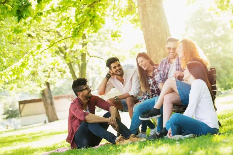 smiling young people sitting on grass beside tree