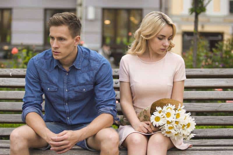 Unhappy couple sitting after arguing, girl with flowers, relationship problem