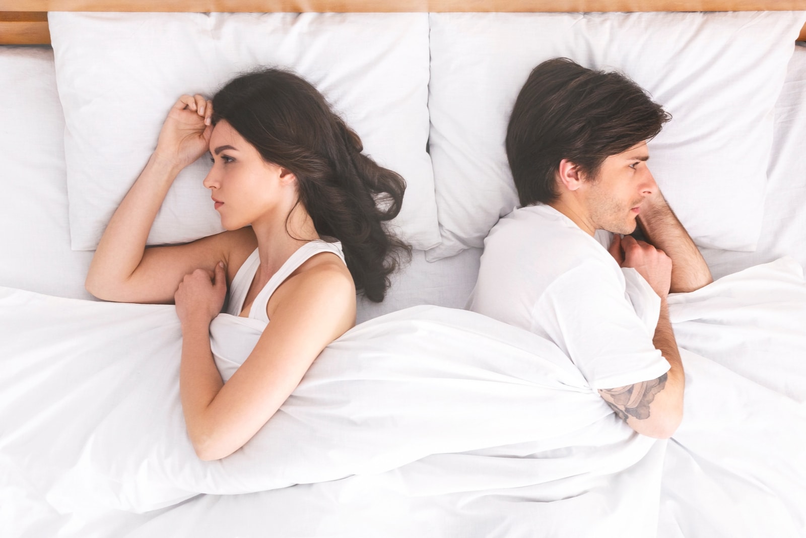 Una coppia sconvolta che si ignora a vicenda, sdraiata schiena contro schiena nel letto