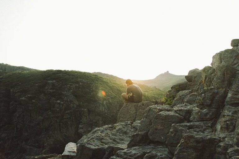 man sitting alone on rock hill