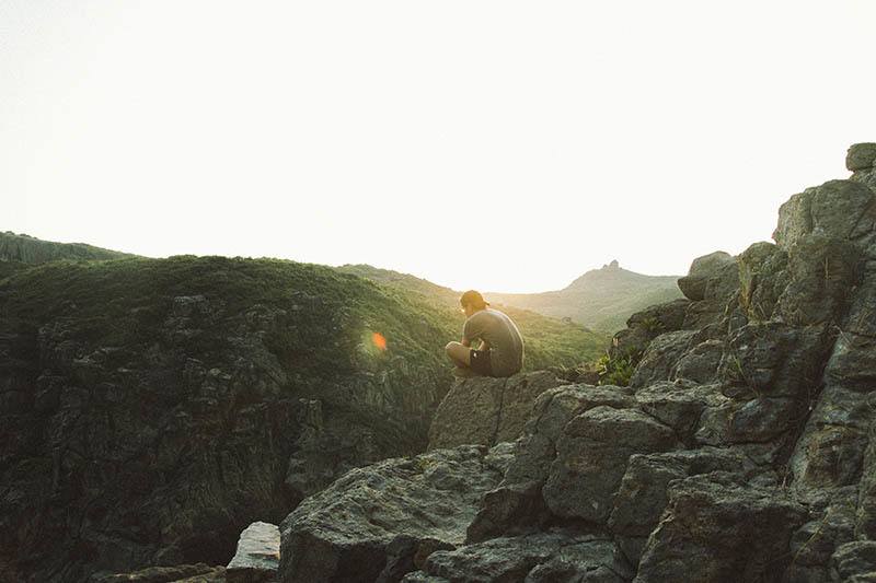 man sitting alone on rock hill