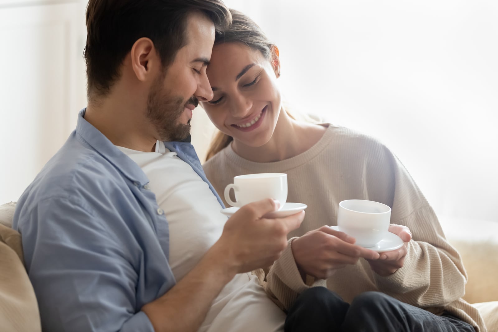 a happy couple in love sitting on a sofa and drinking coffee