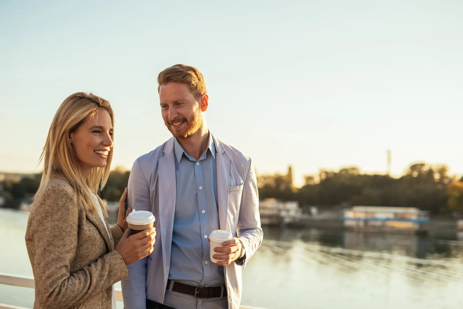 a man and a woman stand with coffee in their hands and talk