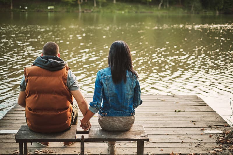 coppia che si tiene per mano e siede in riva al lago