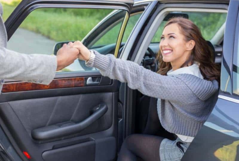 uomo tiene per mano una donna sorridente mentre scende dall'auto