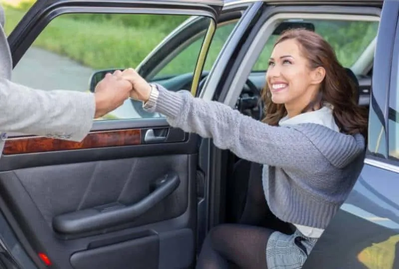 man holds smiling woman hand while she getting out of car