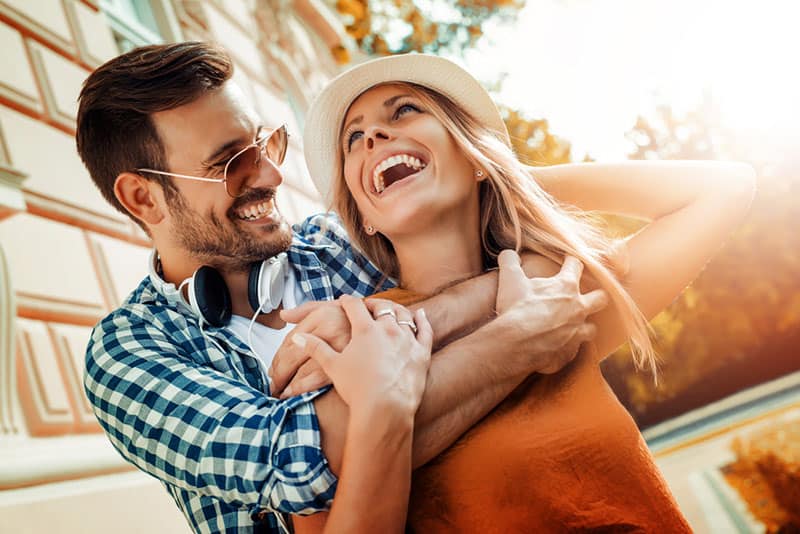 hombre abrazando a mujer sonriente de espaldas al exterior