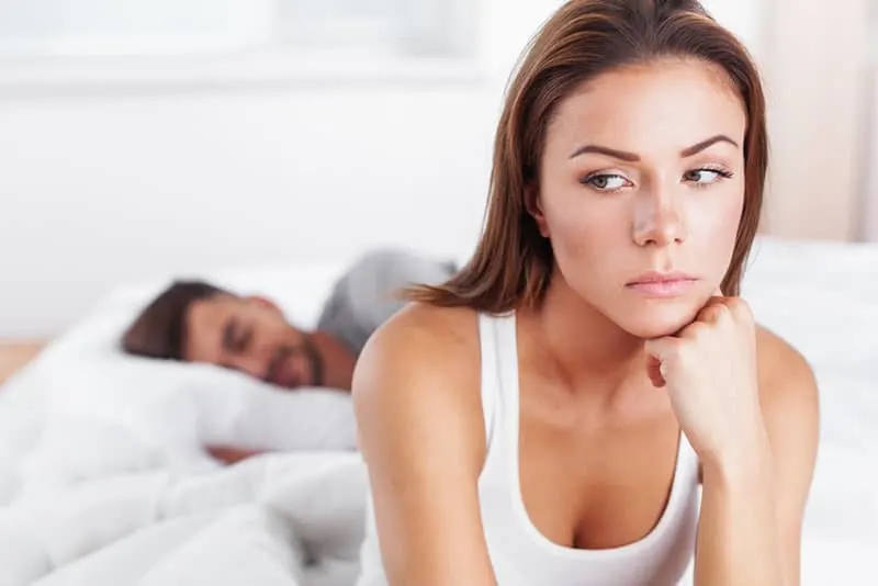 sad woman looking away while man sleeping