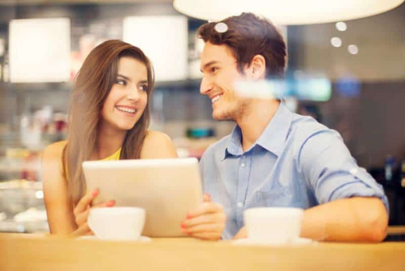 casal sorridente sentado e a olhar um para o outro num café