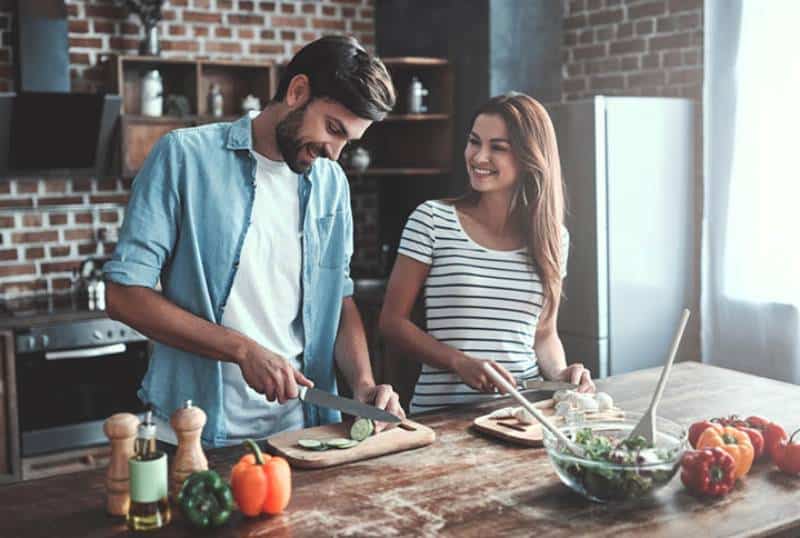 sonriente pareja de jóvenes cocinando juntos en casa