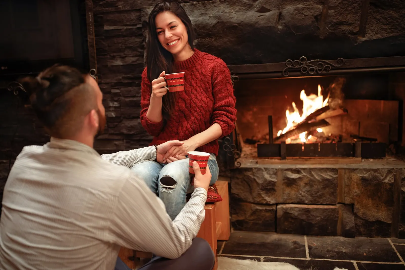 the man holds the woman's hand as they sit by the fire