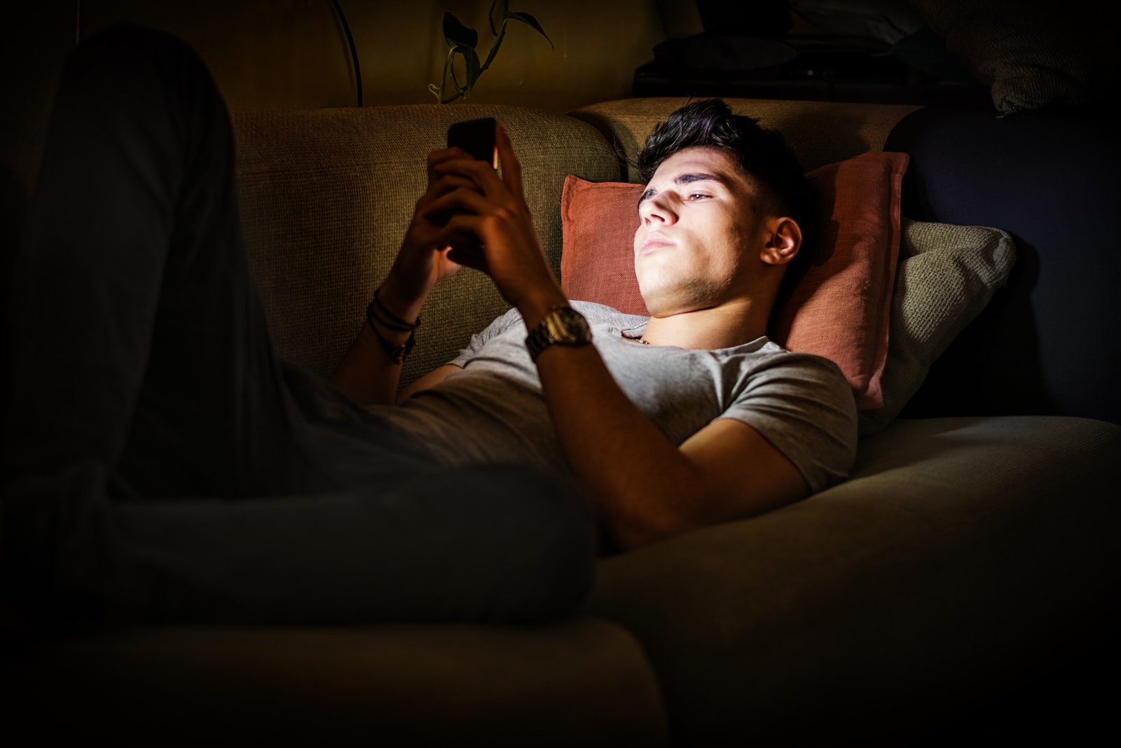 the young man is lying on the couch and using a smartphone