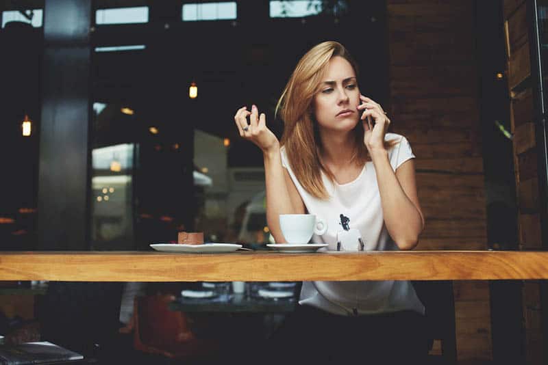 woman looks thoughtful while talking on phone at cafe