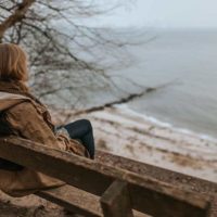 mulher sentada sozinha num banco em frente ao mar