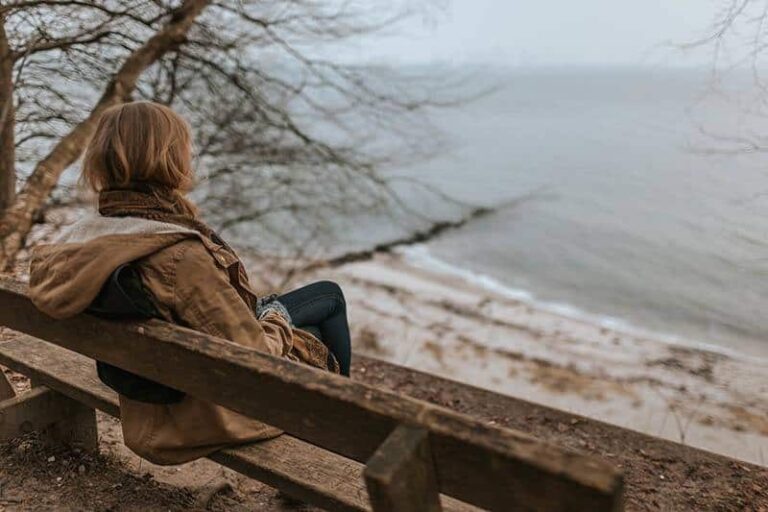 woman sitting alone on a bench in front of sea