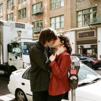 couple kisses on sidewalks beside cars