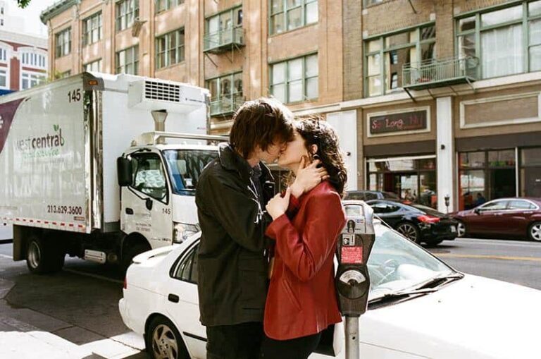 couple kisses on sidewalks beside cars