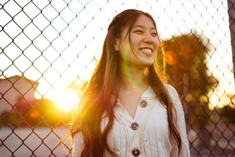 Woman smiling in front of chain link fence during golden hour