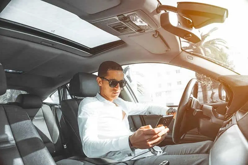 man wearing sunglasses and blue shirt typing on his phone