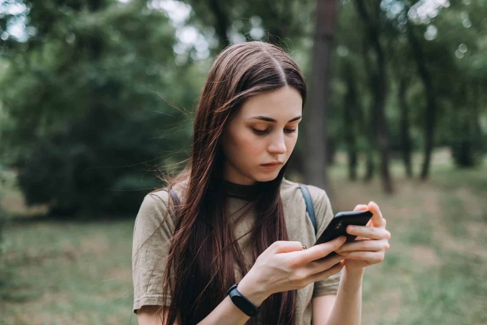 mujer en el parque de la ciudad sola, usa un smartphone