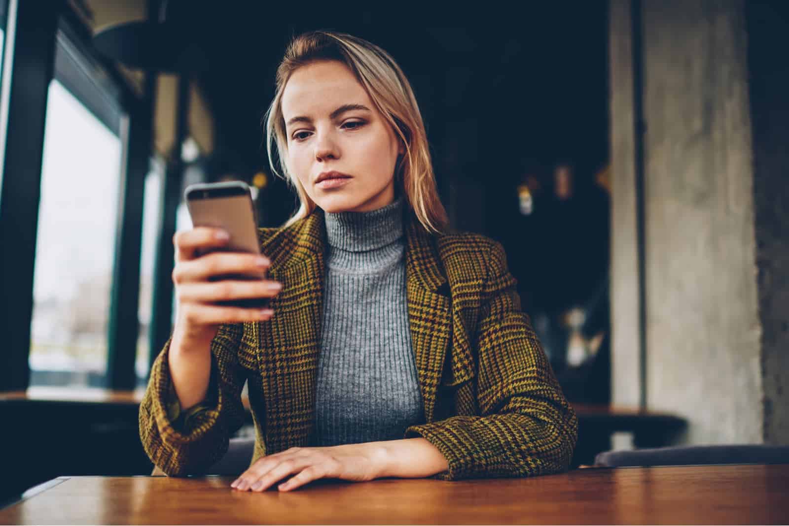 mulher sentada junto à mesa com o telemóvel na mão