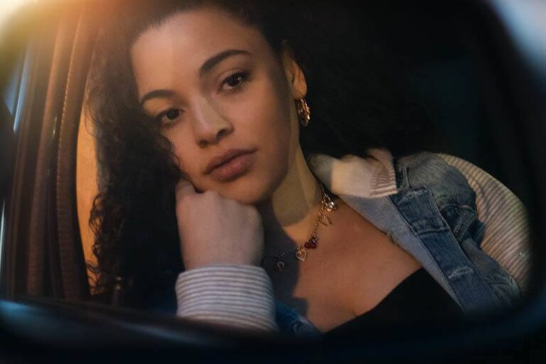 thoughtful woman with curly hair leaning on car window
