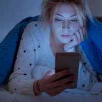 disappointed woman holding her phone while lying on bed