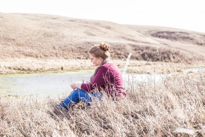 Woman sitting on grass next to concrete road in the day